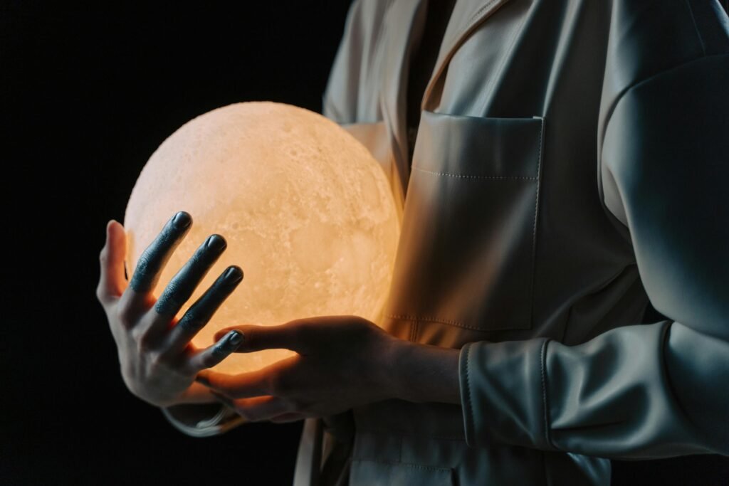 A person in a reflective pose holding a glowing sphere against a dark studio background.